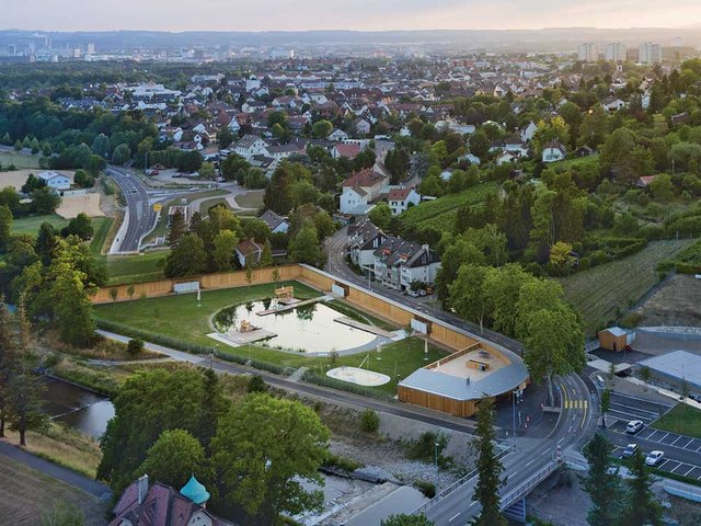 Zur Strasse hin wird das Bad von einer hölzernen Umfassungswand abgeschirmt. Der Blick in die Auenlandschaft ist frei.