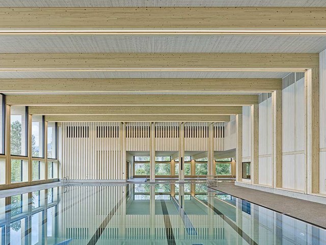 Zwillingsträger aus Brettschichtholz mit innen liegender Beleuchtung überspannen das Schwimmerbecken.Die gelochten Dreischichtplatten an der Decke sorgen für eine erstaunlich gute Akustik. 