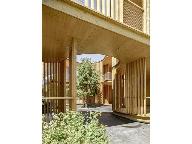Eingangsbereich, der zum Innenhof führt. Dieser verbindet die beiden einzelnen Baukörper des Kindergartens. Durch die einheitliche Materialisierung mit Holz wirkt der Bau als harmonisches Ganzes. Links zu sehen die Rutschbahn, die sich vom Obergeschoss in den Hof windet. 