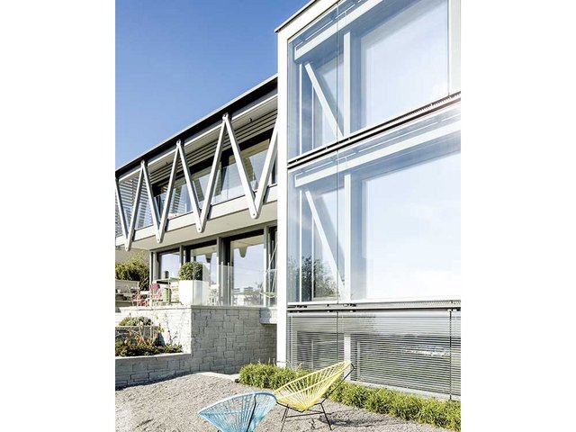 Ein Projekt, zwei Baukörper: Die beiden Volumen unterscheiden sich in der konstruktiven Ausformulierung der Elemente. Das Haus auf der Westseite hat grosse Vordächer und eine aussenliegende Tragstruktur als Aufhängung der Laube. Das ostseitige Volumen lässt die Tragstruktur hinter der grosszügigen Verglasungen sichtbar werden.