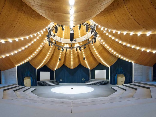 Orientalische Formensprache, ein multifunktionaler Raum und in Form gebogenes Holz: Das vereint der Zauberhut. Im Mittelpunkt steht sein spektakuläres Schalentragwerk. Vierhundertfünfzig, in aufwendiger Geometrie erstellte, gelochte Fichtenplatten garantieren eine hervorragende Raumakustik. 