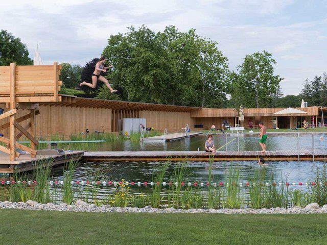Mit Schwung vom Sprungturm: Helles Lärchenholz, Wasserpflanzen und grüner Rasen dominieren das Bild des Naturbads – von buntem Plastik keine Spur.